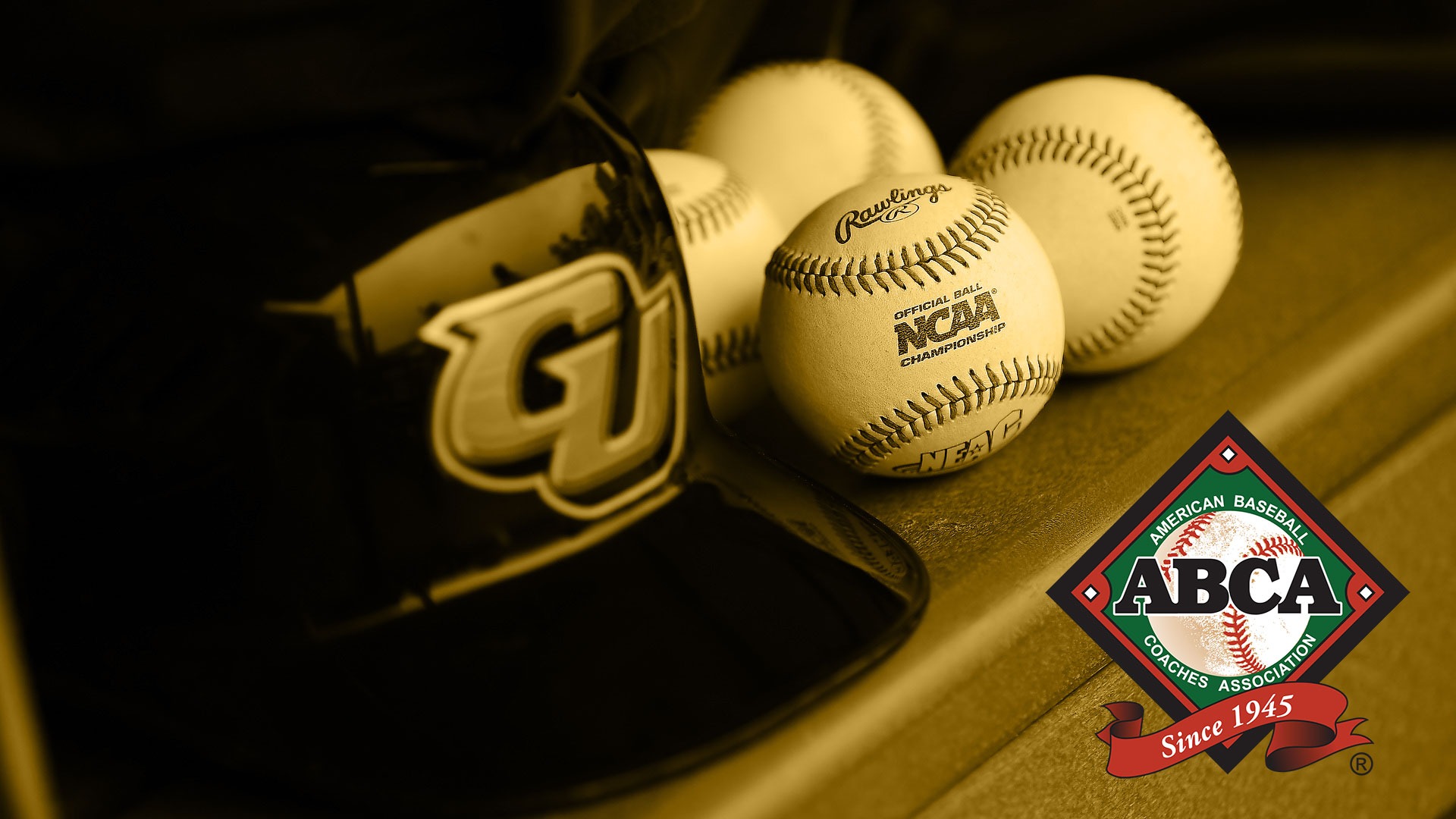 GU Baseball Helmet sits on the bench in the dugout of Hoy Field. A set of baseballs sit next to the helmet. An ABCA (American Baseball Coaches Association) logo is in the lower righthand corner. The entire photo has a gold filter on it except for the red/black/green ABCA logo.