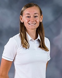 2023 WSOC Headshot - Sabina Shysh - Women's soccer assistant coach looks towards the camera for a headshot. The coach is wearing a white collared Bison shirt. There is a gray backdrop behind the coach.