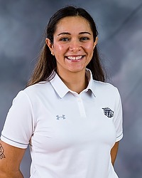 2023 WSOC Headshot - Stephanie Bettencourt - Women's soccer volunteer coach looks towards the camera for a headshot. The coach is wearing a white collared Bison shirt. There is a gray backdrop behind the coach.