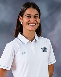 2023 WSOC Headshot - Eve Wood-Jacobowitz - Women's soccer assistant coach looks towards the camera for a headshot. The coach is wearing a white Bison collared shirt. There is a gray backdrop behind the coach.