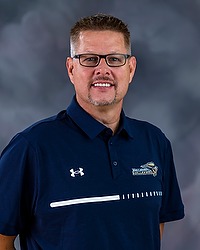 2023 WVB Headshot - Lynn Ray Boren - Women's volleyball head coach looks towards the camera for a headshot. The coach is wearing a blue collared Bison shirt. There is a gray backdrop behind the coach.