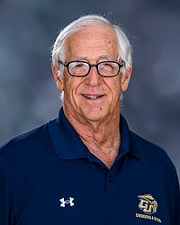 Gallaudet men’s & women's swimming 2024-25 Larry Curran. The coach is wearing a navy blue polo shirt with a GU Bison logo. The coach is photographed with a gray background in the back.