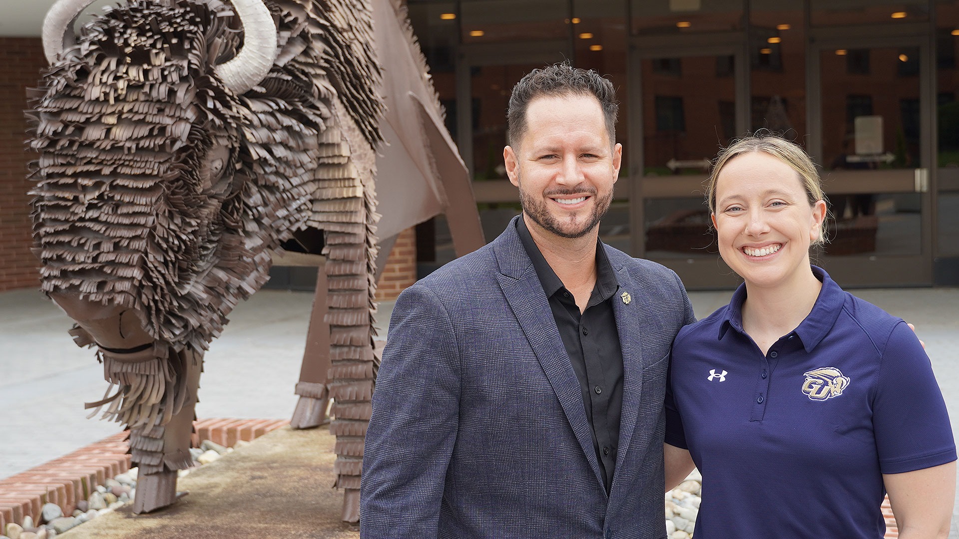 20240513-stunt-headcoach-daze-celine GU Athletic Director Warren Keller (left) stands next to STUNT Head Coach Celine Daze in front of the Mighty Bison Statue in front of the Field House.