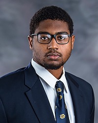 Abu Saccoh 2024 Gallaudet University football headshot. Football player looks towards the camera for a headshot. The player is wearing a white collared shirt with a blue bison tie under a navy blue blazer. There is a gray backdrop behind the player.