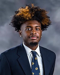 KaVargio Smith 2024 Gallaudet University football headshot. Football player looks towards the camera for a headshot. The player is wearing a white collared shirt with a blue bison tie under a navy blue blazer. There is a gray backdrop behind the player.