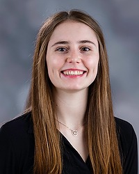 Skyla Baird - 2025-26 Gallaudet women’s basketball headshot. The Bison coach wears a black blouse and looks towards the camera. A gray backdrop is in the background.