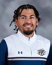 2025-26 Gallaudet University women's basketball team manager Matthew Flores headshot photo. he is wearing a white and navy blue pullover against a grey background.