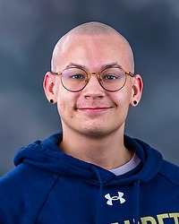 2025 MVB Headshot - Martin Skjeveland- Men's volleyball manager looks towards the camera for a headshot. The manager is wearing a blue Bison hoodie. There is a gray backdrop behind the player.