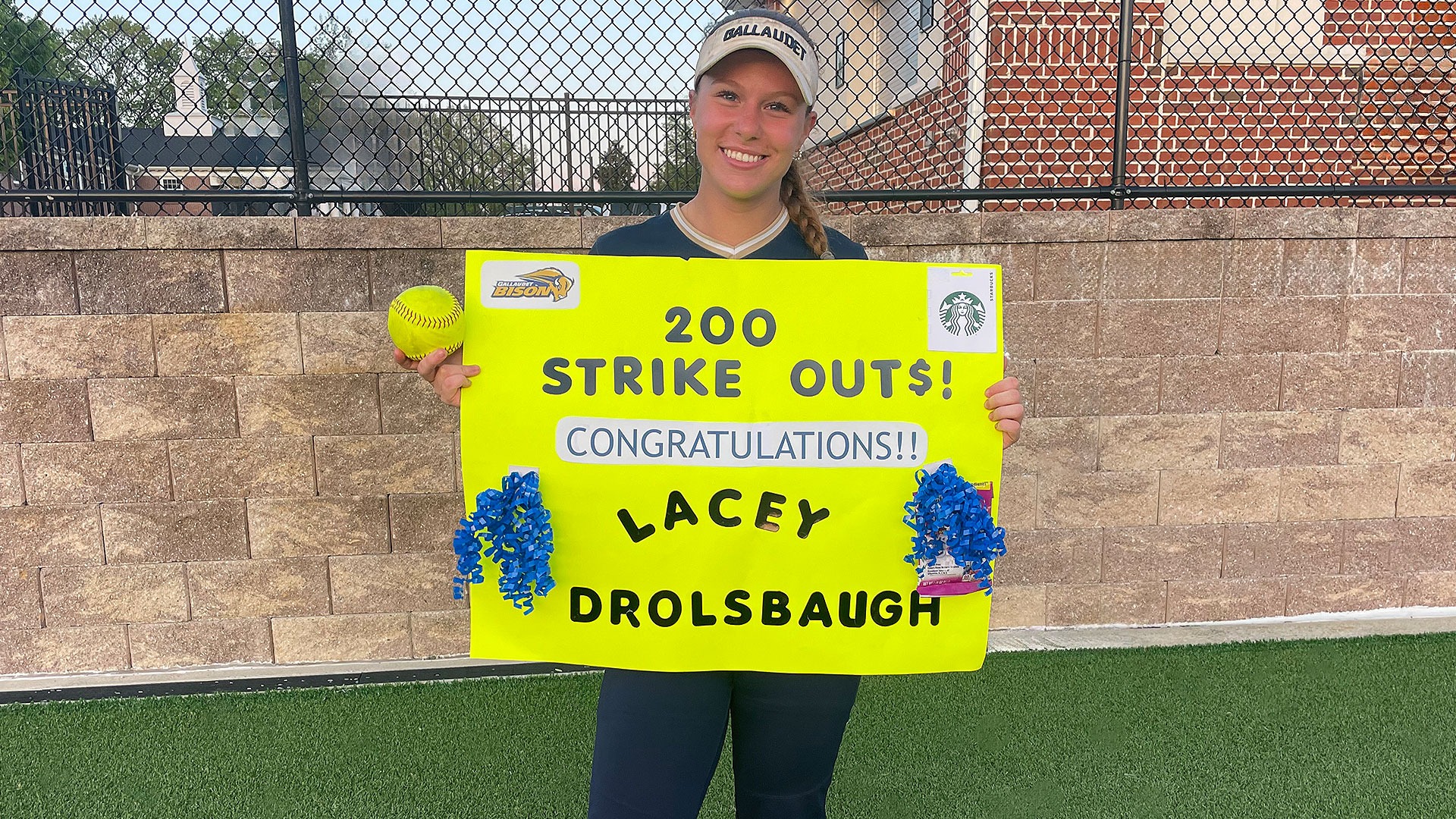 Gallaudet softball pitcher Lacey Drolsbaugh holds up a sign that reads 200 strikeouts, Congratulations Lacey Drolsbaugh. 