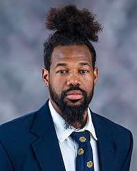 Christopher Webb 2025 Gallaudet University football headshot. Football coach looks towards the camera for a headshot. The coach is wearing a white collared shirt with a blue bison tie under a navy blue blazer. There is a gray backdrop behind the coach.