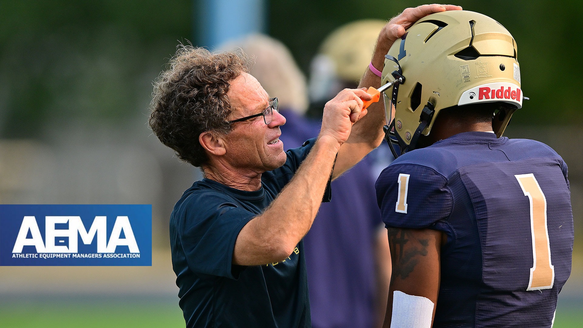 Gallaudet's Kris Gould fixes a Bison football helmet before the start of a home game late in the evening at Hotchkiss Field. An AEMA - Athletic Equipment Managers Association (AEMA) logo is on the lefthand side.