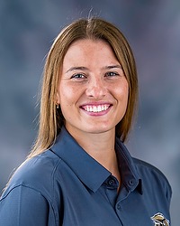 2025 MSOC Headshot - Cam Lexow - Men's soccer coach looks towards the camera for a headshot. The coach is wearing a grey polo shirt. There is a gray backdrop behind the coach.