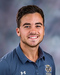 2025 MSOC Headshot - Kyle Santello - Men's soccer coach looks towards the camera for a headshot. The coach is wearing a grey polo shirt. There is a gray backdrop behind the coach.