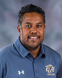2025 MSOC Headshot - Jay Shaw - Men's soccer coach looks towards the camera for a headshot. The coach is wearing a grey polo shirt. There is a gray backdrop behind the coach.