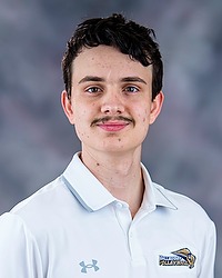 2025 WVB Headshot - Xavier Egbert Women's volleyball manager looks towards the camera for a headshot. The manager is wearing a white polo shirt. There is a gray backdrop behind the player.