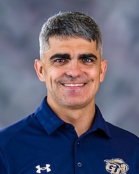 Gallaudet Women's Triathlon 2025 headshot Brian Bennett. The coach is wearing a blue polo shirt. The coach is photographed with a gray background in the back.