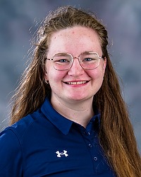 Gallaudet Women's Triathlon 2025 headshot Thea Wrenn. The coach is wearing a blue polo shirt. The coach is photographed with a gray background in the back.
