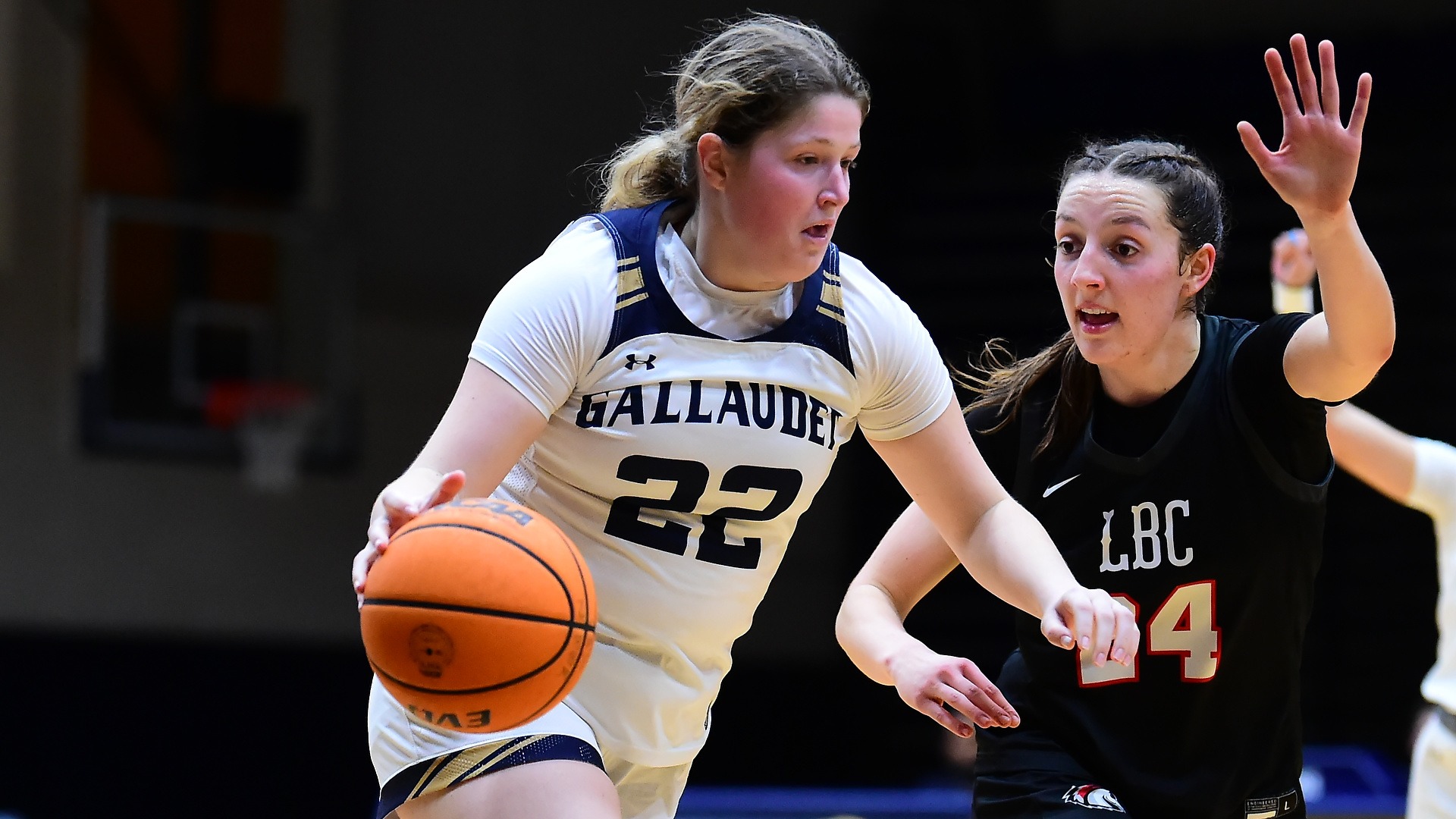 Gallaudet women's basketball player Mackenzie Schirg drives past a Lancaster Bible College defender during a home game in the Field House. The Bison team is wearing their home white uniforms.