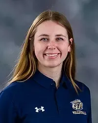 Ella Gamble - 2026 Gallaudet men’s volleyball headshot. The Bison student-assistant coach wears a navy colored polo and looks towards the camera. A gray backdrop is in the background.