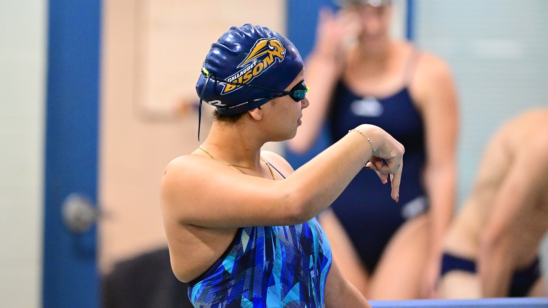 Gallaudet women's swimmer Youstina Alesha signs to a teammate before the start of an event as Alesha stands on the pool deck.