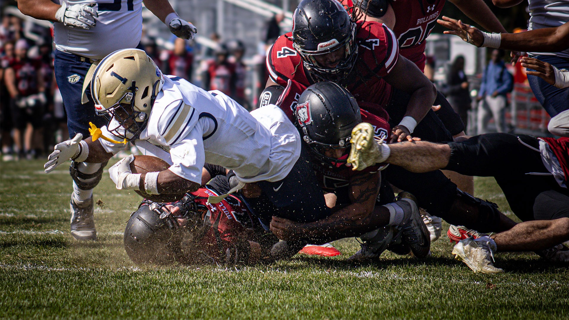Gallaudet football running back Marcus Brown-Gabriel (#1) plunges forward with the ball tucked tightly against his chest as several Dean College Bulldogs defenders converge to make the tackle, kicking up dirt and grass during Saturday's game on Oct. 10, 2026, in Franklin, Massachusetts.