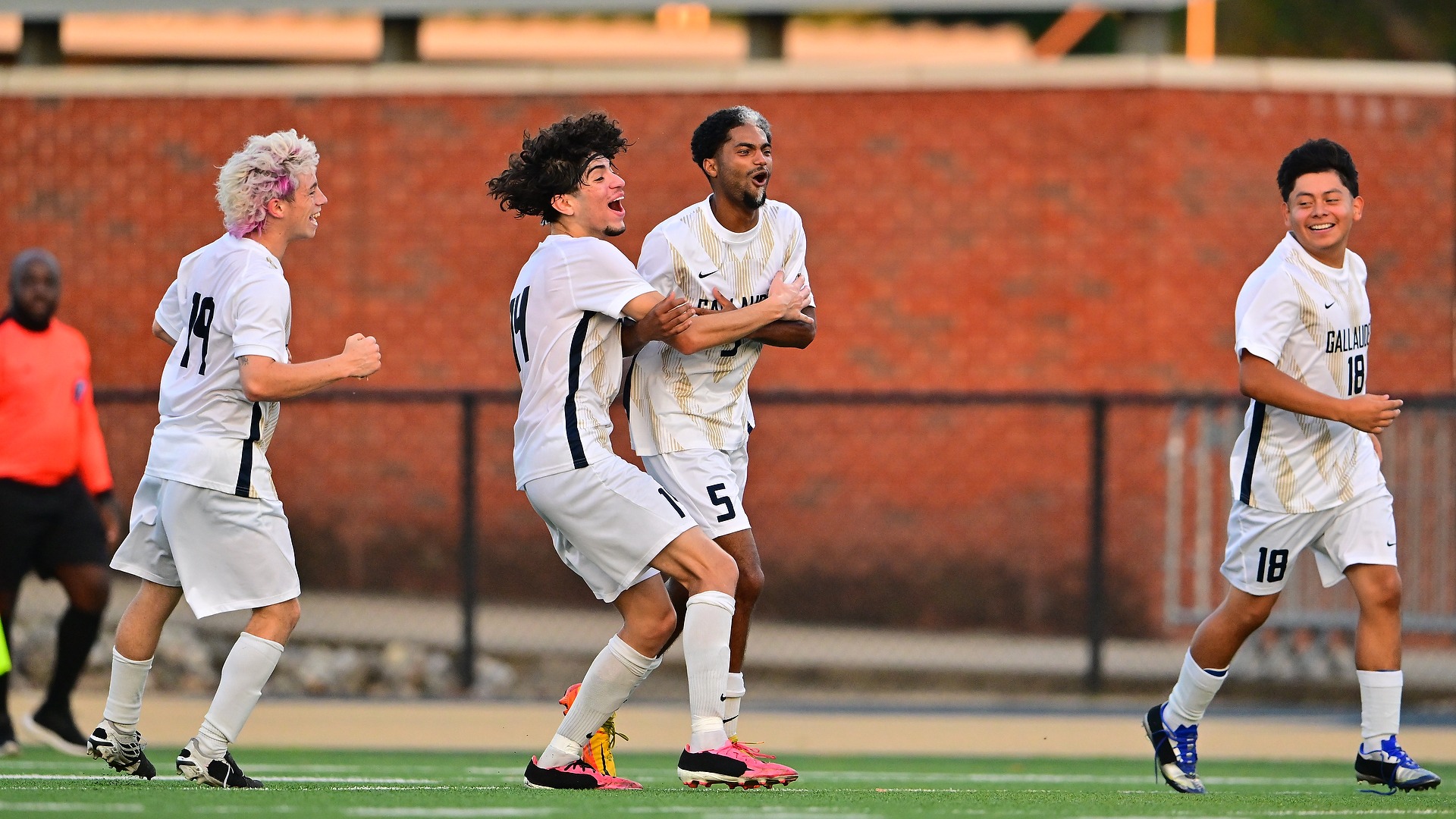 Gallaudet men's soccer player Bruce Brewer Jr. (#5), center, celebrates scoring the Bison's lone goal against Cairn University on Oct. 16 at Hotchkiss Field. Brewer is embraced by teammate Joe Bryan (#4) as Eli Matamoros (#19) and another Bison teammate (#18) join the celebration in their white-and-gold uniforms during the Homecoming weekend match.