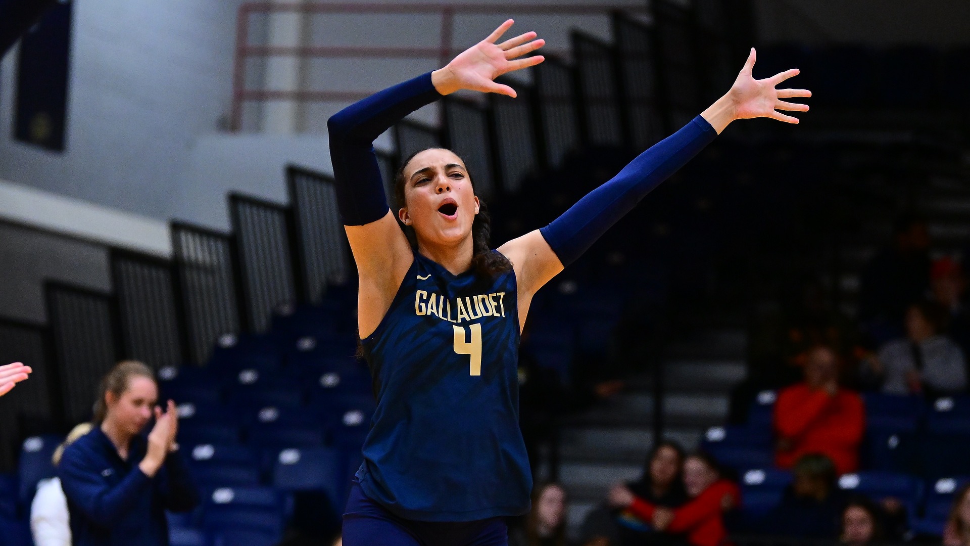 Gallaudet University women’s volleyball player #4 Bri Eilderts celebrates on the court with both arms raised during a match in the Field House.