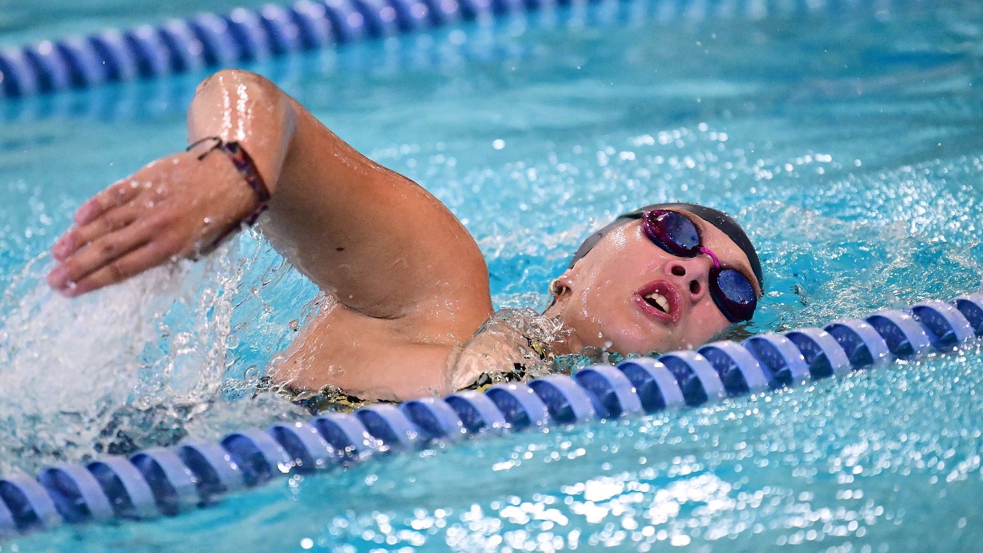 Gallaudet first year Priya Frank swims freestyle in the Field House Pool, turning her head to breathe as she moves through the water between blue-and-white lane lines.