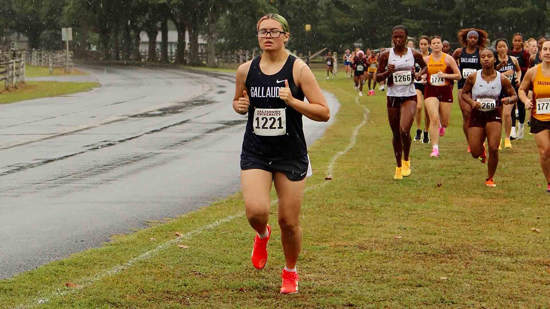 Gallaudet women’s cross country runner Hannah Alford races across the rain-soaked course during Saturday’s Don Cathcart Invitational in Salisbury, Maryland, with a pack of runners following behind her.
