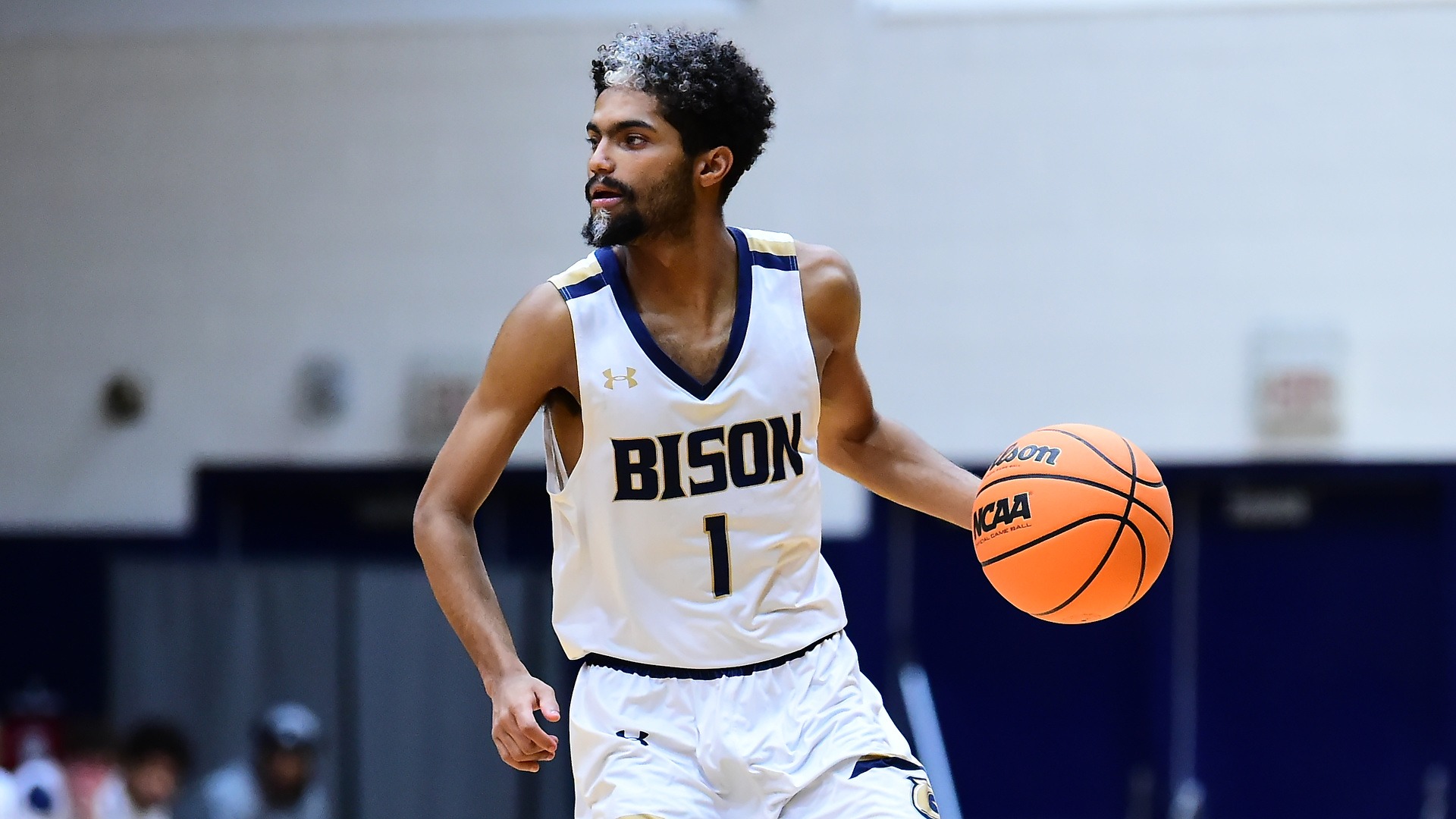 Gallaudet men's basketball guard Bruce Brewer Jr. dribbles and orange NCAA basketball up the court in the Field House during a home contest. Brewer is wearing a white Bison uniform.