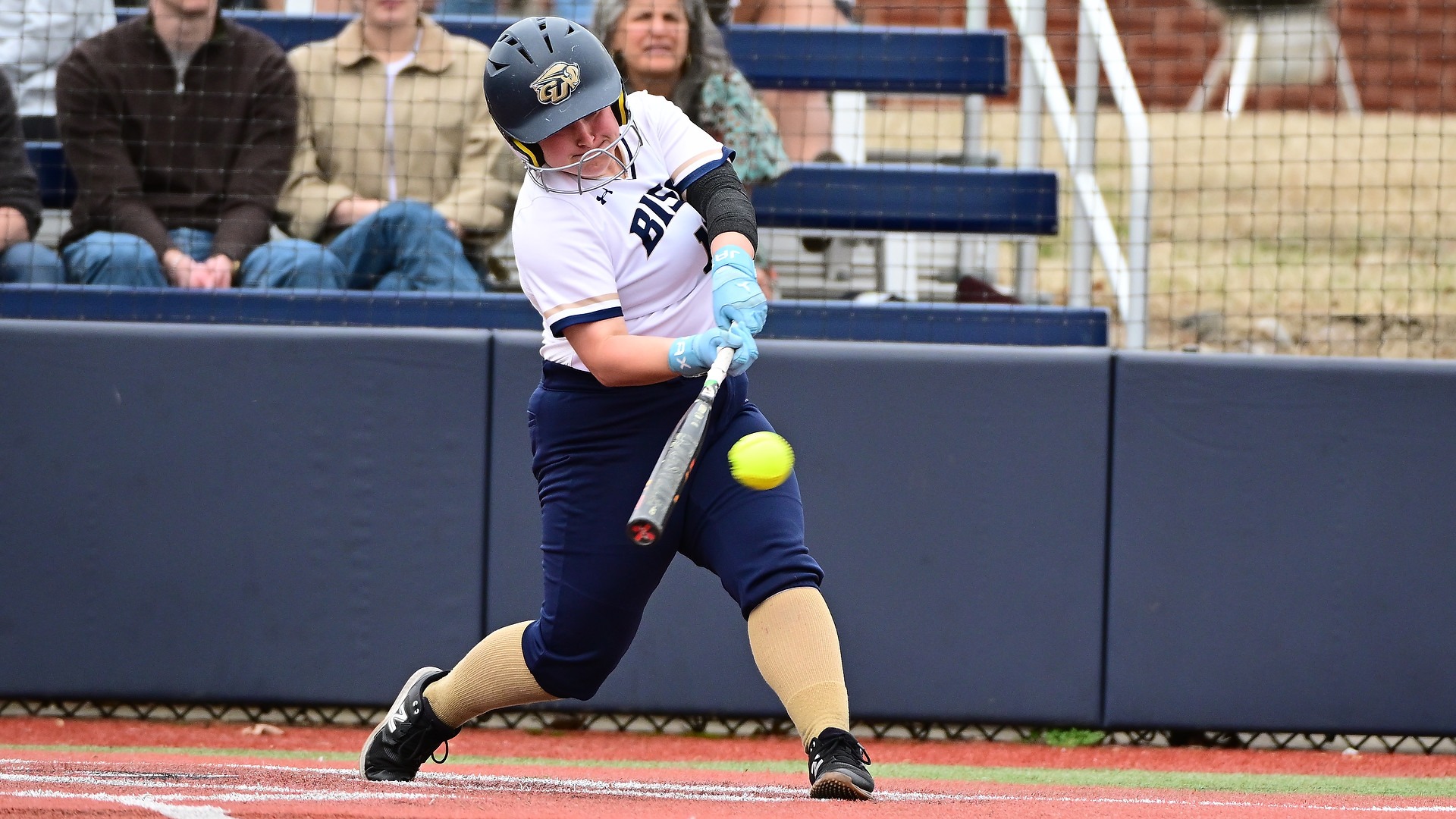 Gallaudet softball player Kinsley Bond swings the bat during a game and makes contact with the neon yellow softball for a hit during the daytime. 