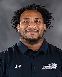 Todd Collins- 2026 Gallaudet women's flag football headshot. The Bison coach wears a black polo shirt and looks towards the camera. A gray backdrop is in the background.