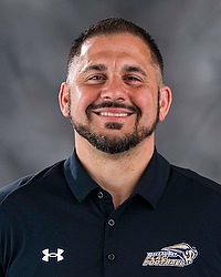 2026 Joseph Kolcun Gallaudet women's flag football headshot. The Bison coach wears a black polo shirt and looks towards the camera. A gray backdrop is in the background.