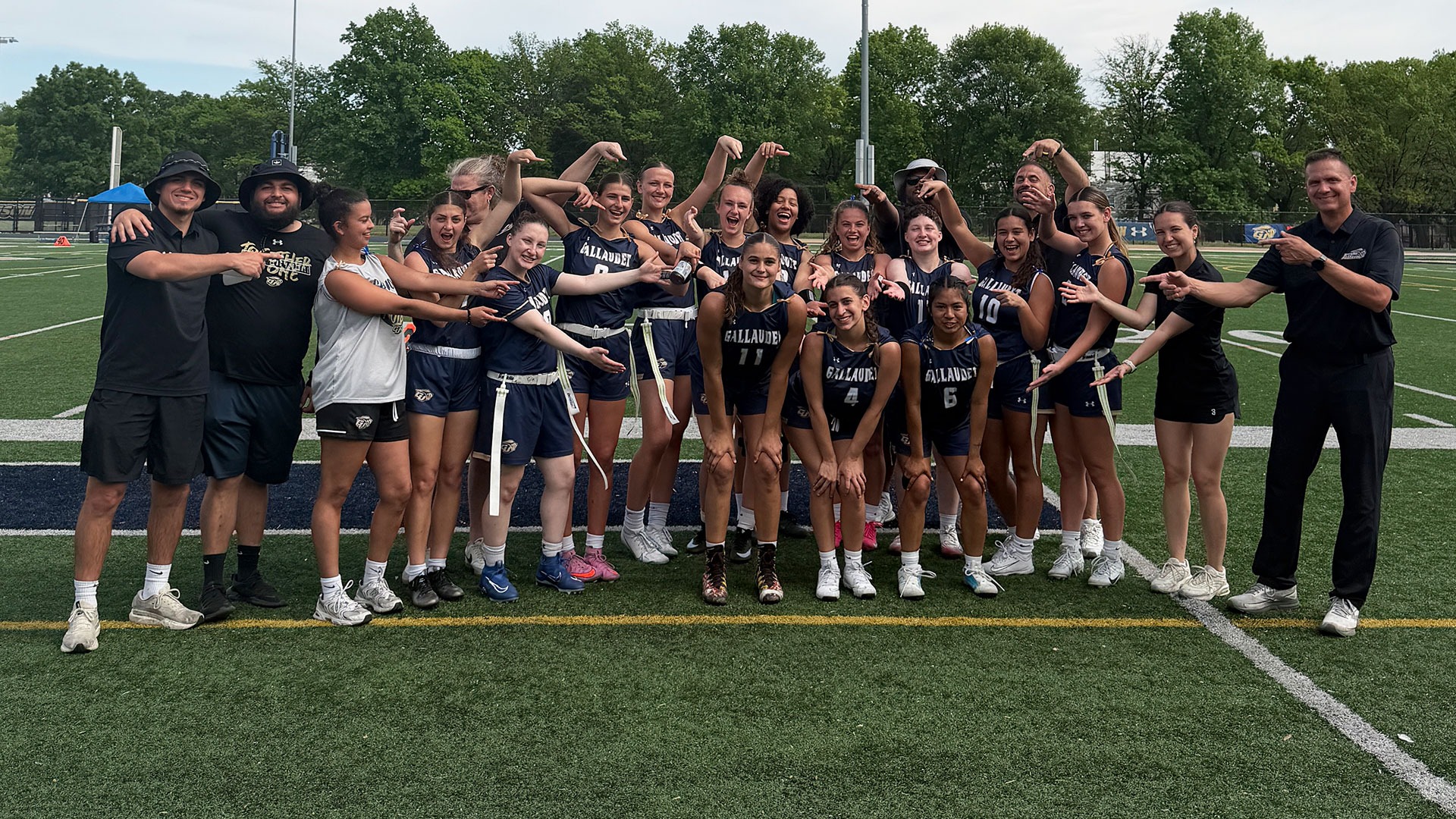 Gallaudet's women's flag football team pose for a fun group photo highlighting their three seniors in the middle of the photo on a sunny day at Hotchkiss Field.