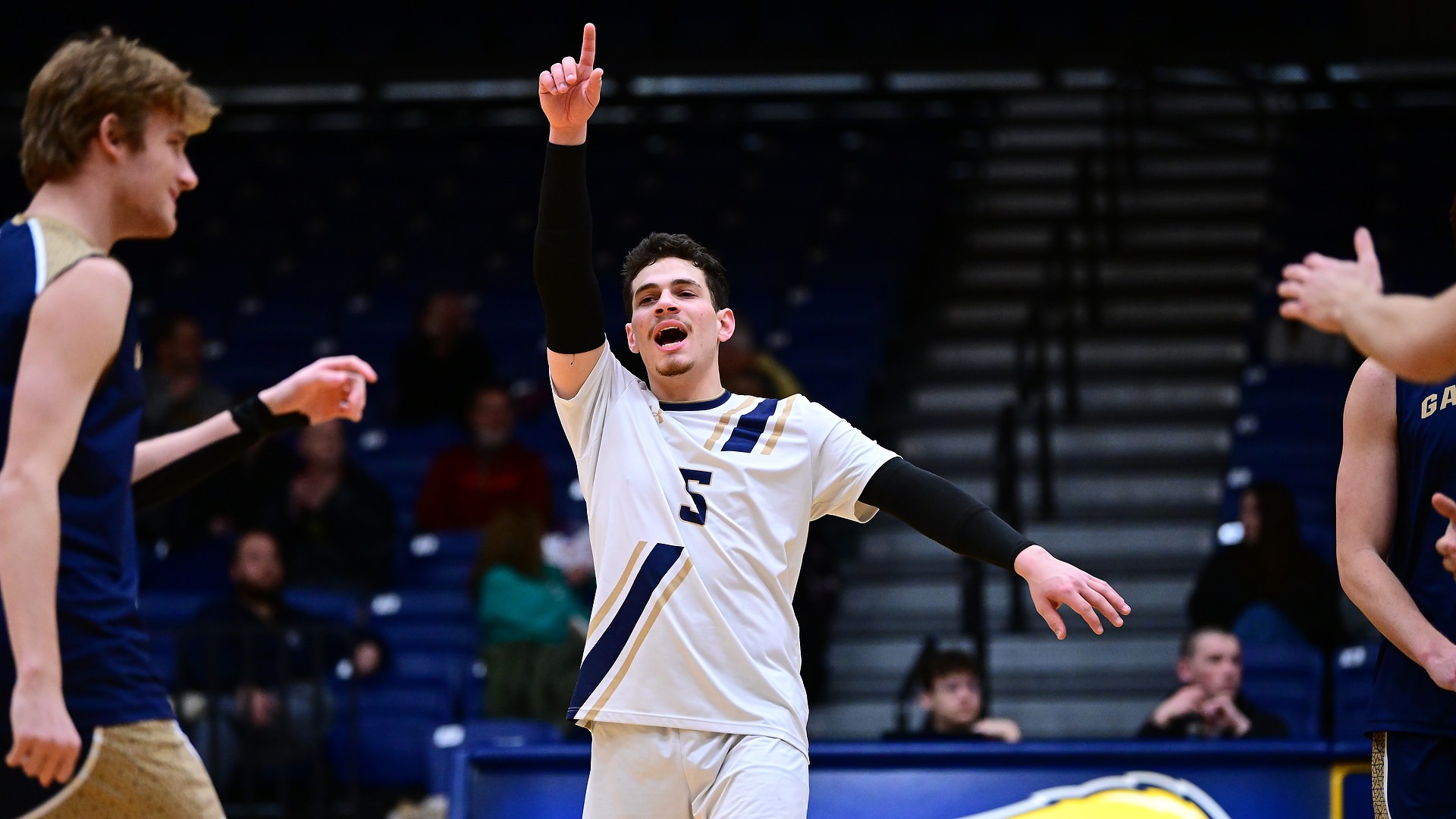 Gallaudet men's volleyball player Elian Zfati celebrates a point by raising his right arm into the air and holding up one finger. 