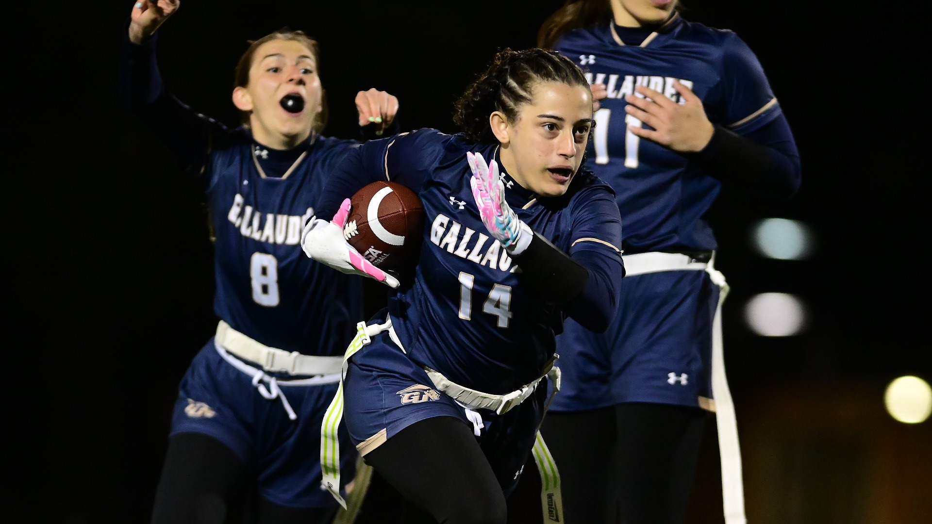 Gallaudet women's flag football player Tamara Tadevosyan rushes the ball in a night game at Hotchkiss Field as her teammates cheer her on.