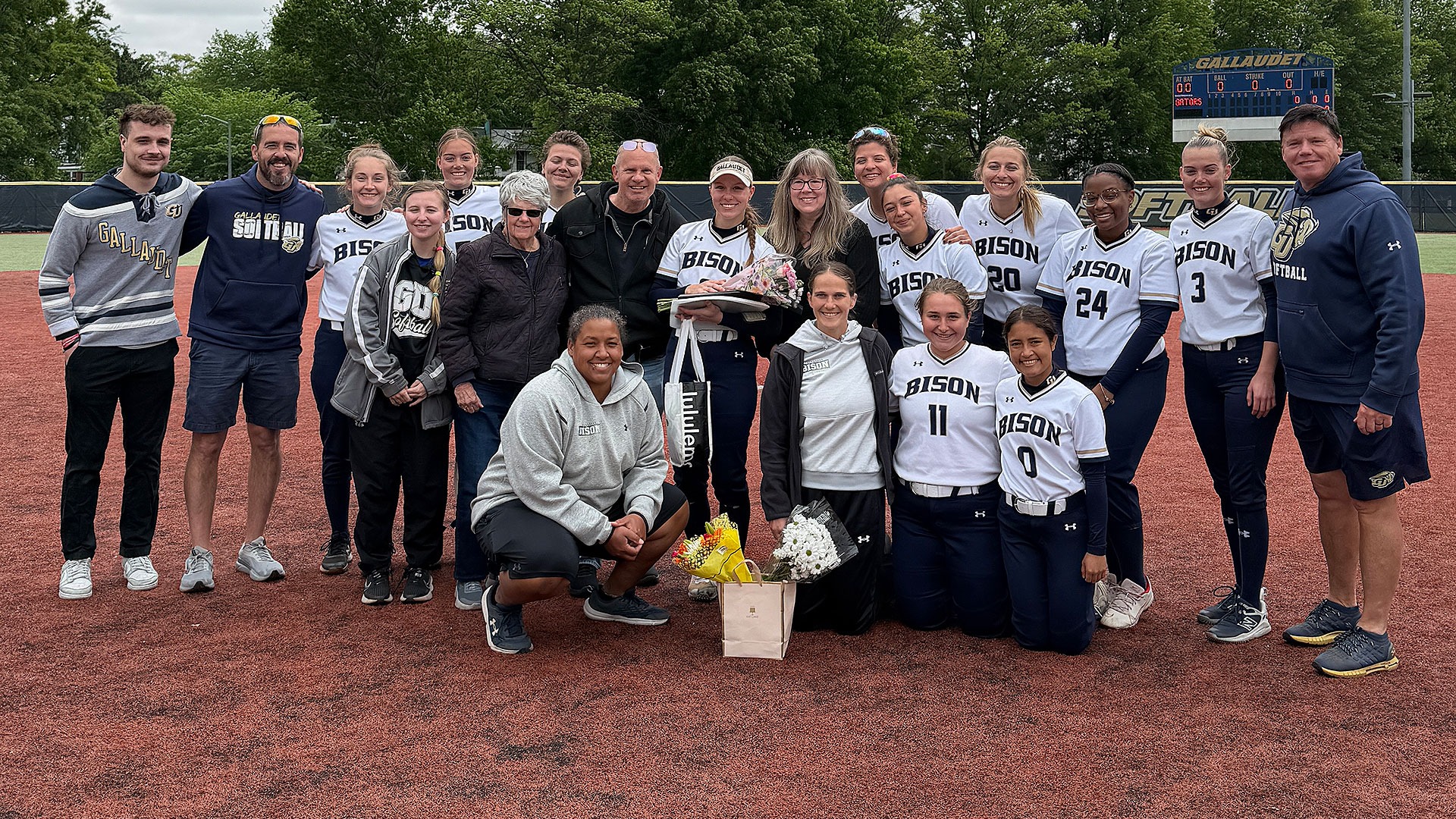 Gallaudet softball team pose for a Senior Day photo with the Drolsbaugh family on an overcast day at the GU Softball Complex.