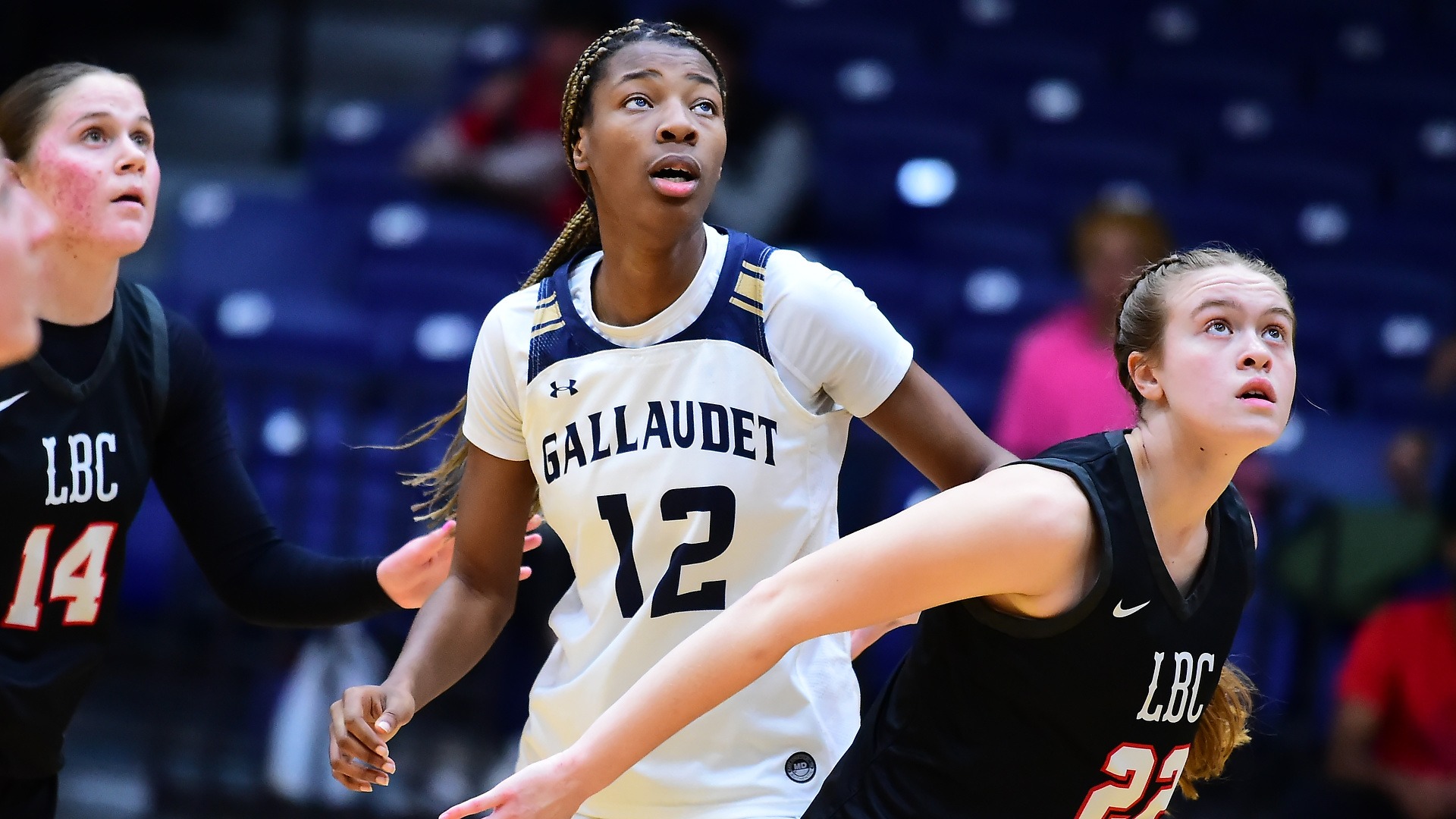 Gallaudet women's basketball player #12 Kayla Debrow looks up at the free throw shot and gets ready to rebound as two Lancaster Bible College defenders are around her.