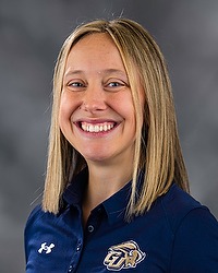 Celine Daze 2026 Gallaudet women's STUNT headshot. The Bison head coach wears a navy colored polo shirt and looks towards the camera. A gray backdrop is in the background.