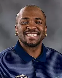 Marquize Nash 2026 Gallaudet women's STUNT headshot. The Bison intern wears a navy colored polo shirt and looks towards the camera. A gray backdrop is in the background.