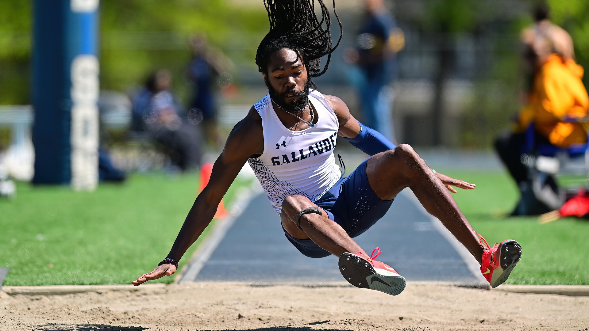 Gallaudet men's track and field jumper Andrae' Green makes a jump and is about to land in the sand pit on a sunny afternoon. 