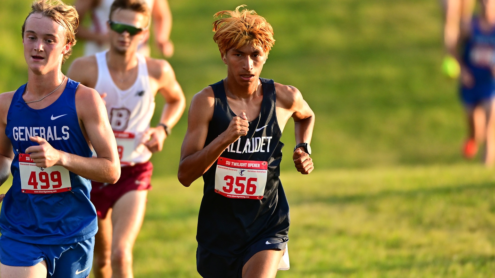 Gallaudet men’s cross country runner Dylan Olmos competes among a pack of runners across a grass field during the SU Twilight Open, illuminated by the warm light of the setting sun Friday evening in Winchester, Virginia.