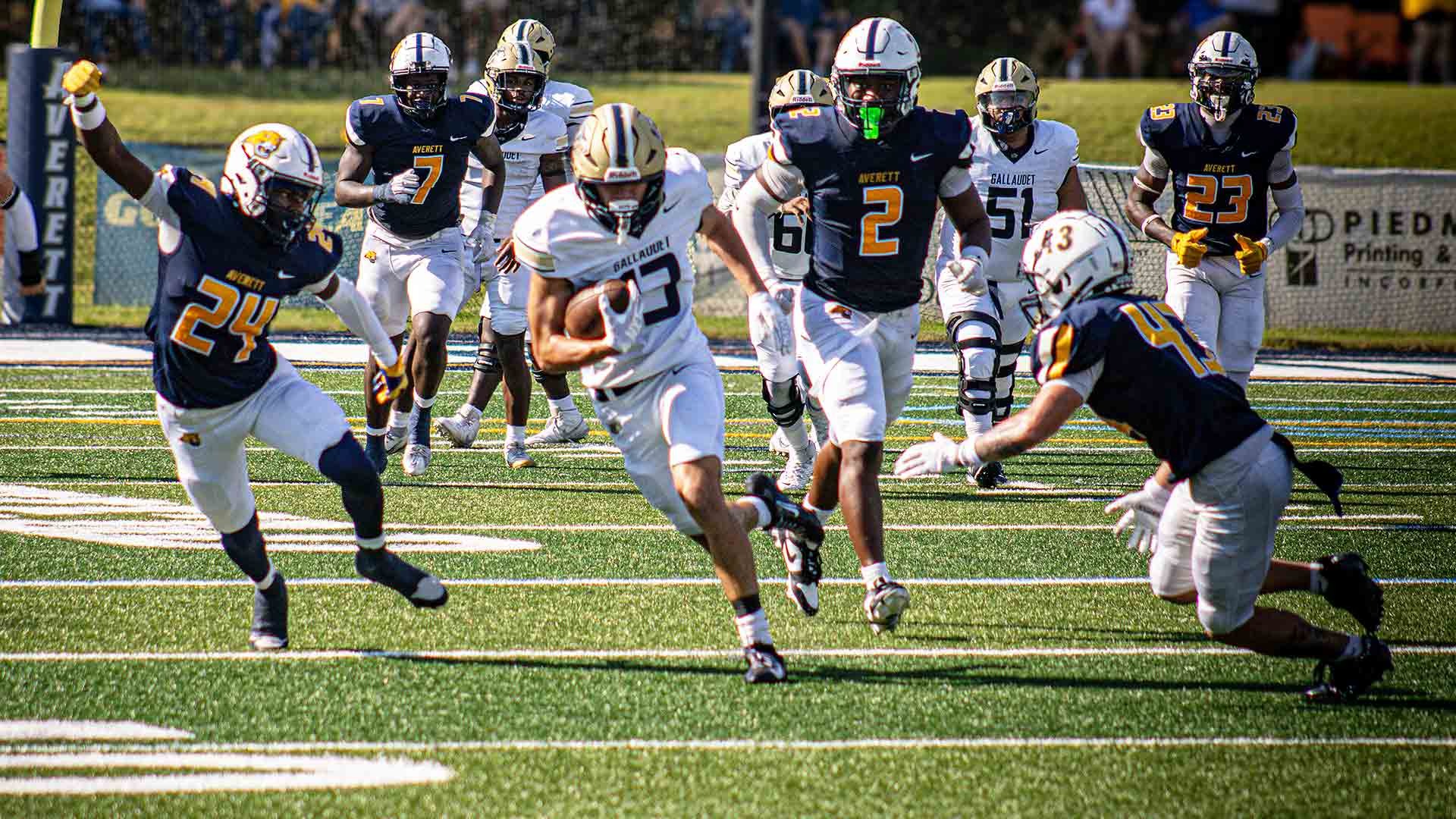 Gallaudet wide receiver Isaiah Baxter (#13), wearing the Bison’s white road uniform and gold helmet, carries the football upfield after a reception as several Averett defenders pursue him during Saturday’s game in Danville, Virginia.