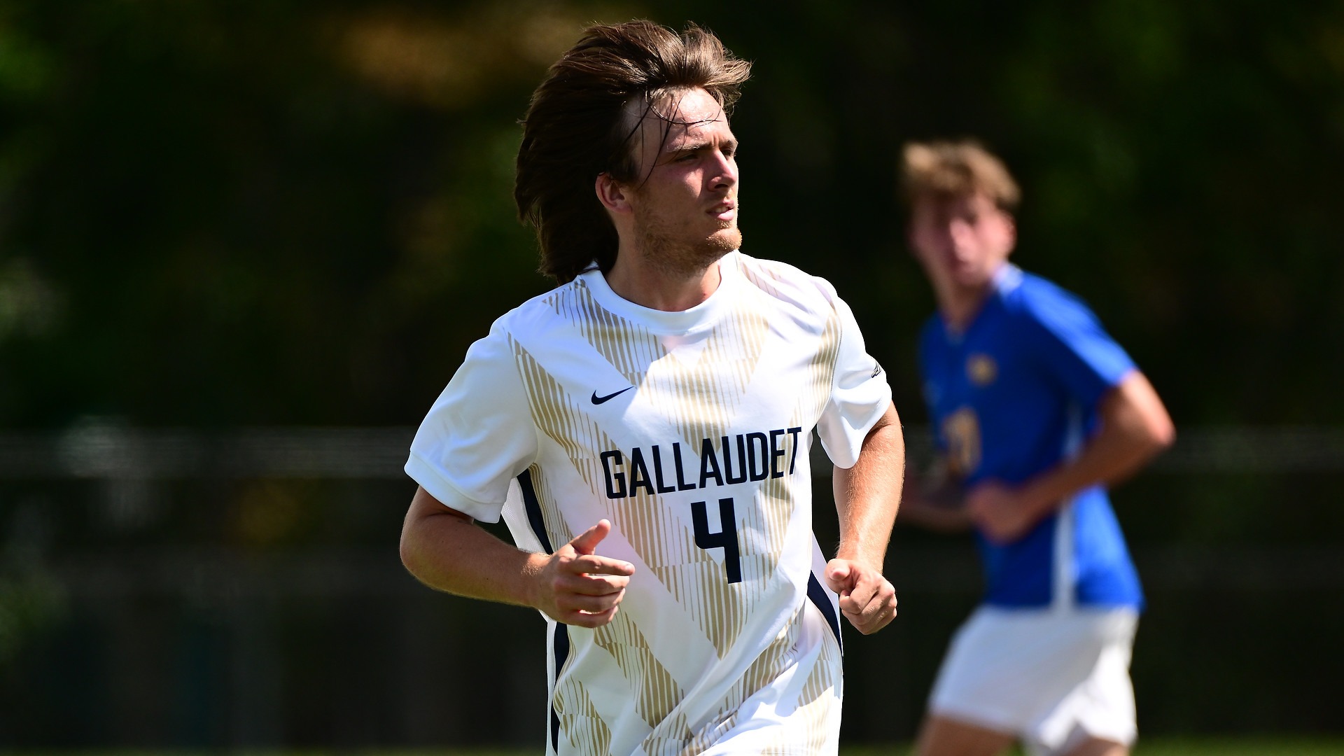 Gallaudet men's soccer player Joe Bryan (#4) runs back on defense in his white-and-gold Bison uniform during a match on a sunny afternoon at Hotchkiss Field.