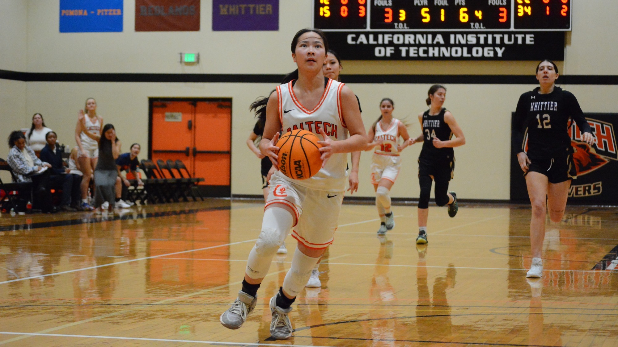 Isabella Lo collects the ball with both hands in front of her as she prepares to rise up for an uncontested driving layup facing the under-the-hoop camera. 