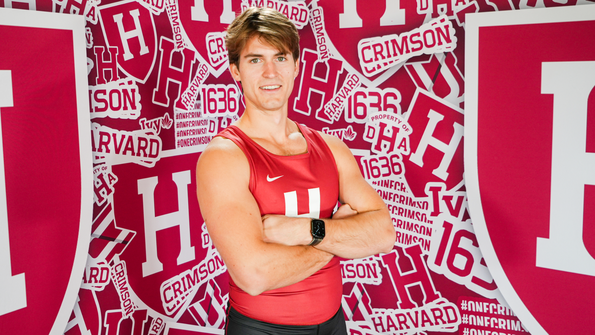 Cameron McInroy standing with arms crossed in front of a Harvard backdrop