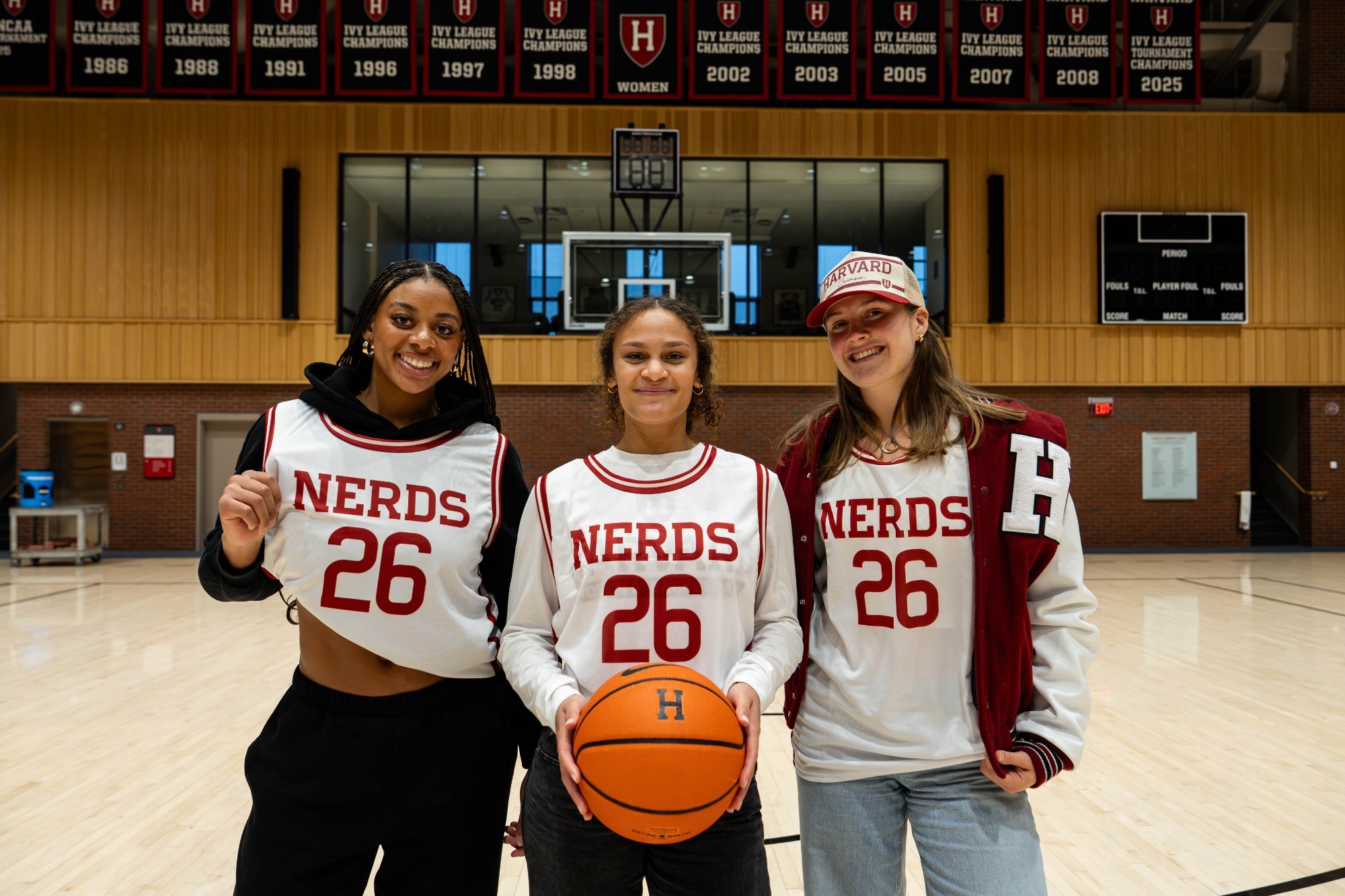 Sophomore Hana Belibi, Junior Karlee White, and Junior Abigail Wright sporting jerseys Harvard fans will receive on January 10