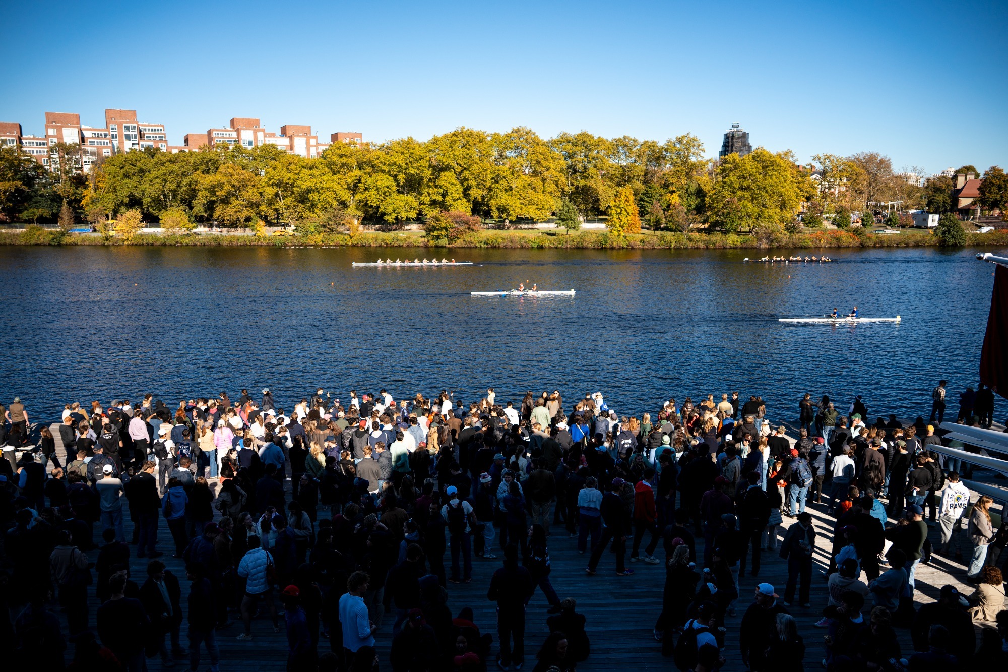 Boats row past a crowd on the Newell Boathouse dock during the 2026 Head of the Charles Regatta.