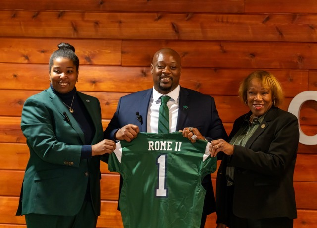 Coach Rome II stands with President Scott and Dr. Carroll, holding a Chicago State University football jersey.