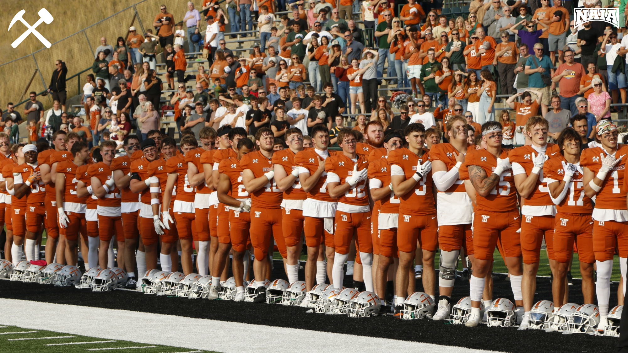 Montana Tech's football team stands on the sideline saluting the flag during the national anthem